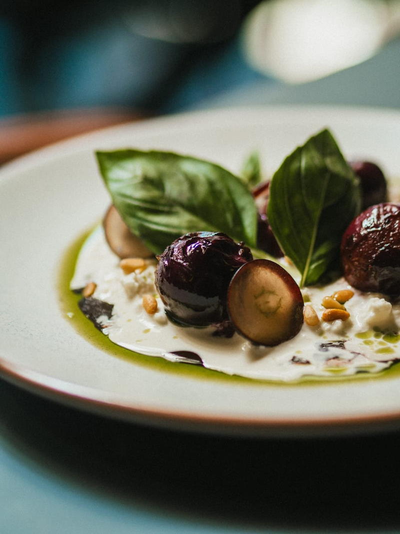 Grapes, basil and pine nuts over stracciatella on a white plate.